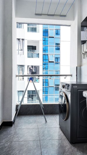 Un cuarto de lavandería con lavadora, tendedero y vistas a un edificio con ventanas azules.