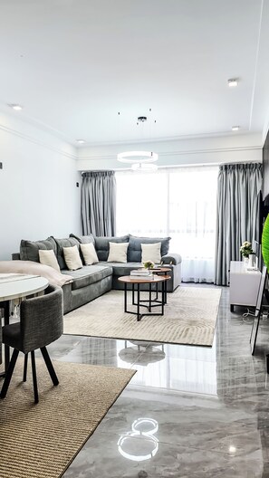 Ein modernes Wohnzimmer mit einem grauen Sofa, einem runden Couchtisch und einem Essbereich mit einem weißen Tisch und Stühlen.