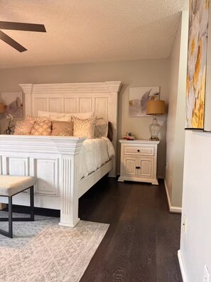 A bedroom with a white bed, a nightstand, a lamp, and a painting on the wall. - Wellington Polo Tranquility (Wellington)