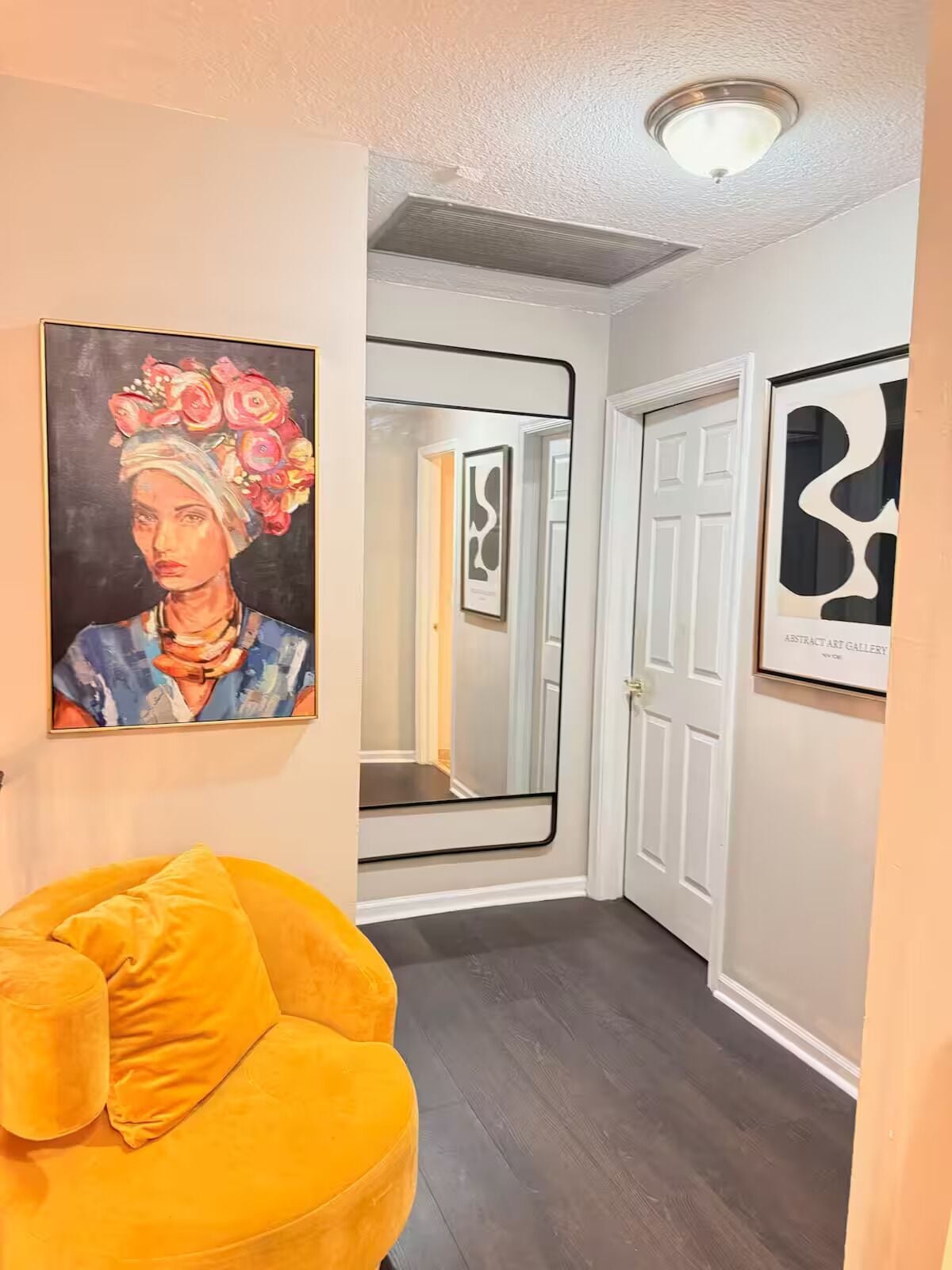 Un pasillo con una silla amarilla, un cuadro y una puerta que da a una habitación.