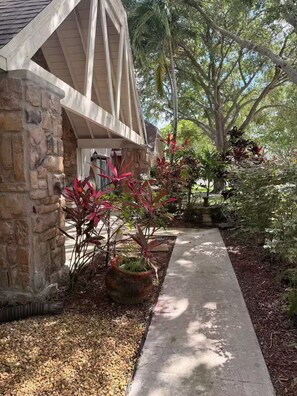 A pathway leading to a stone building with a sloped roof and a garden with various plants. - Wellington Polo Tranquility (Wellington)