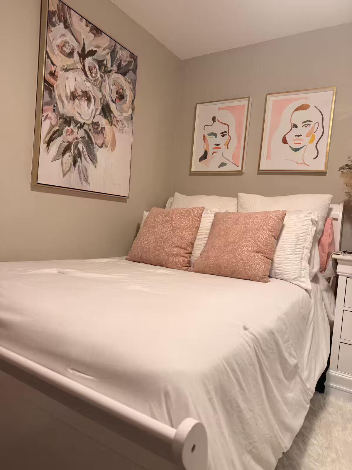 Ein Schlafzimmer mit Bett, Kissen, Nachttisch und Wandbildern.
