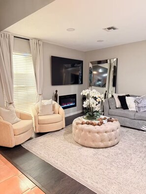 A modern living room with a fireplace, two armchairs, a sofa, a round ottoman, and a flat-screen TV. - Wellington Polo Tranquility (Wellington)