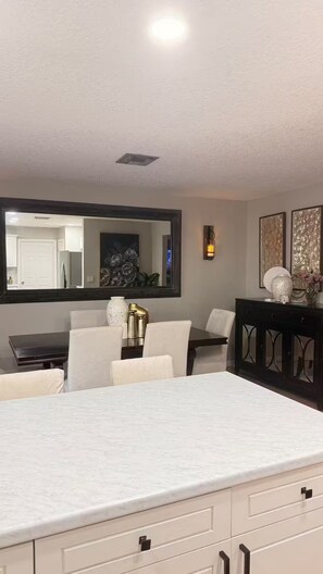 A modern kitchen with a marble countertop, a dining area with a large mirror, and a dark wooden cabinet. - Wellington Polo Tranquility (Wellington)