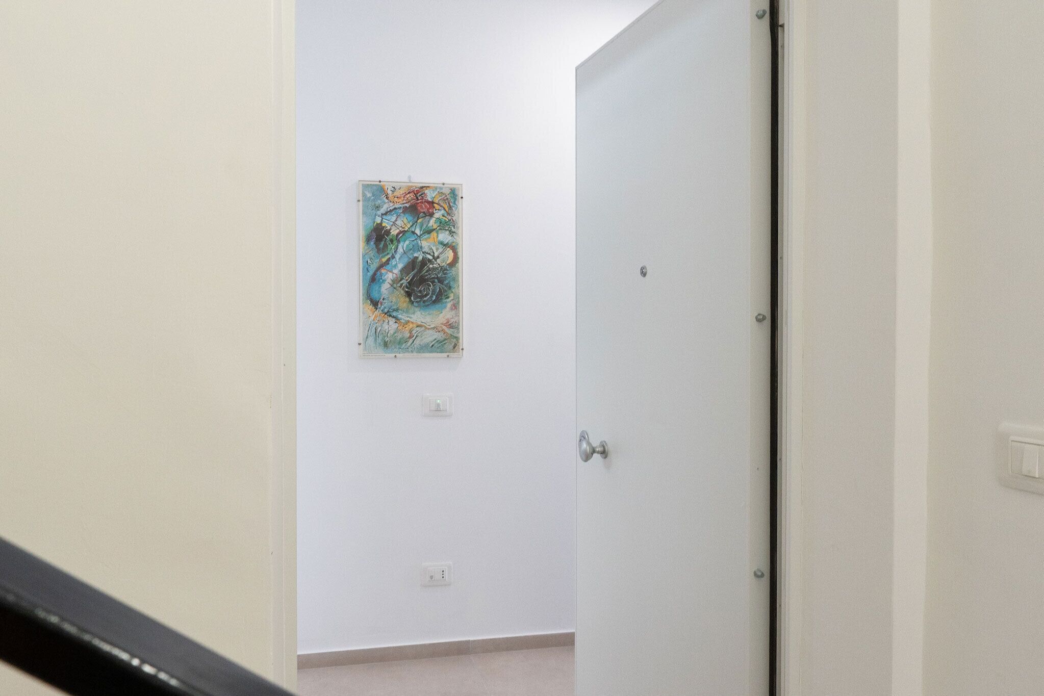 Un pasillo con una puerta blanca, un interruptor de luz y un enchufe en la pared.