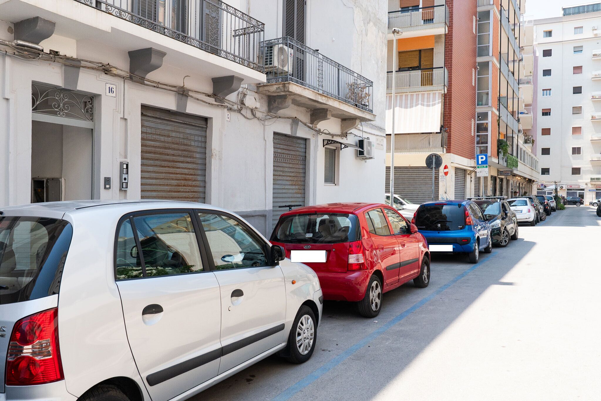 Una fila de coches estacionados a lo largo de una calle urbana, con edificios a ambos lados.