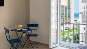 Un balcón con mesa y sillas, vista al mar, y un edificio con andamios.