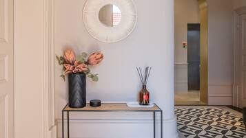 A hallway with a black and white patterned floor, a white console table with a vase of flowers, a mirror, and a door with a sign.