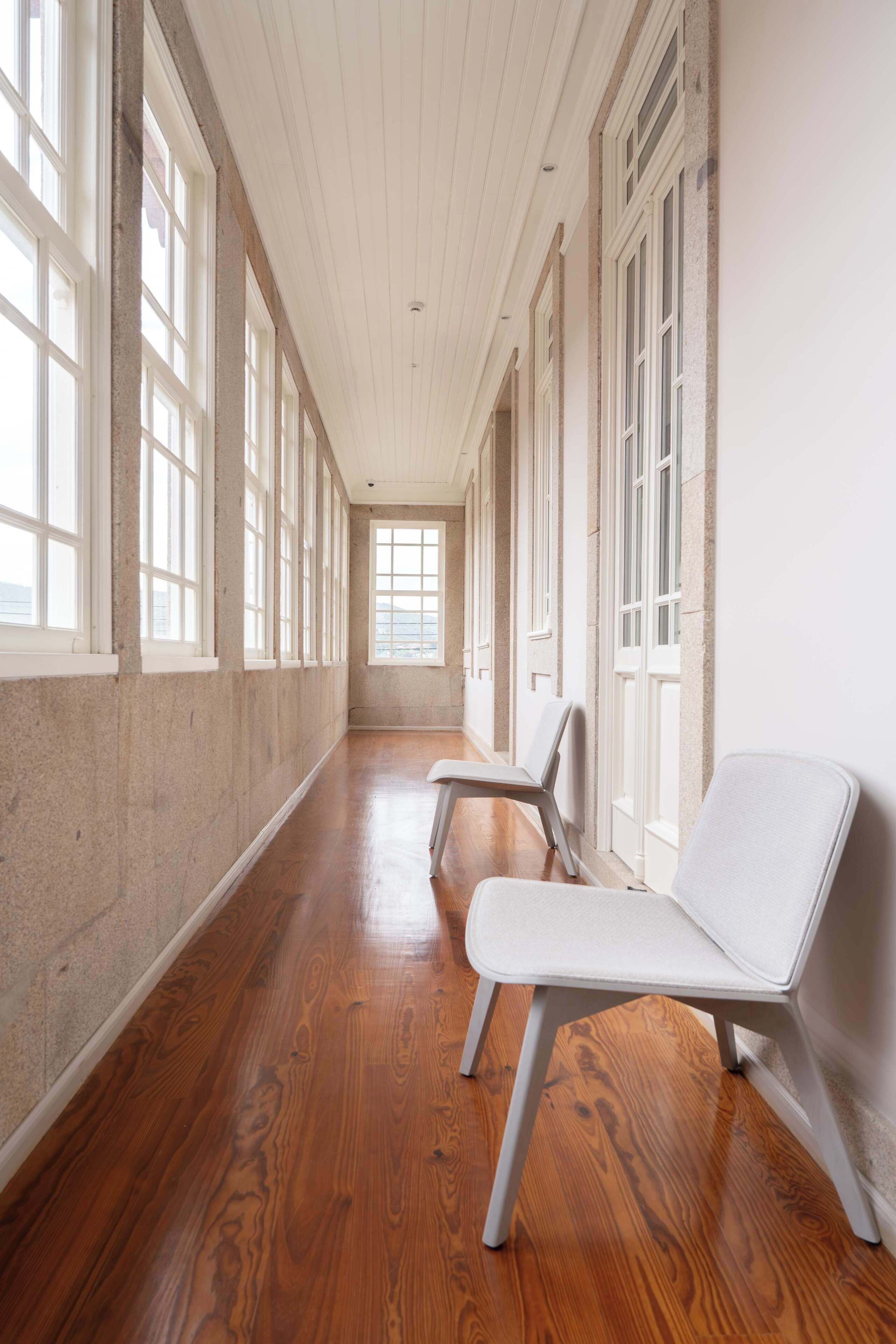 A long hallway with wooden floors, white walls, and large windows.