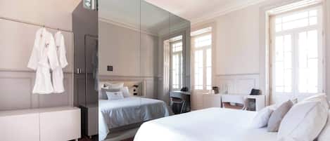 A hotel room with a large bed, a desk, a mirror, and a wardrobe.