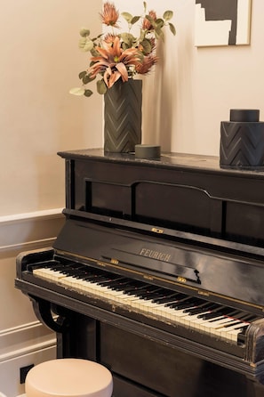Ein schwarzes Klavier mit weißem Hocker, eine Vase mit Blumen und ein gerahmtes Bild an der Wand.