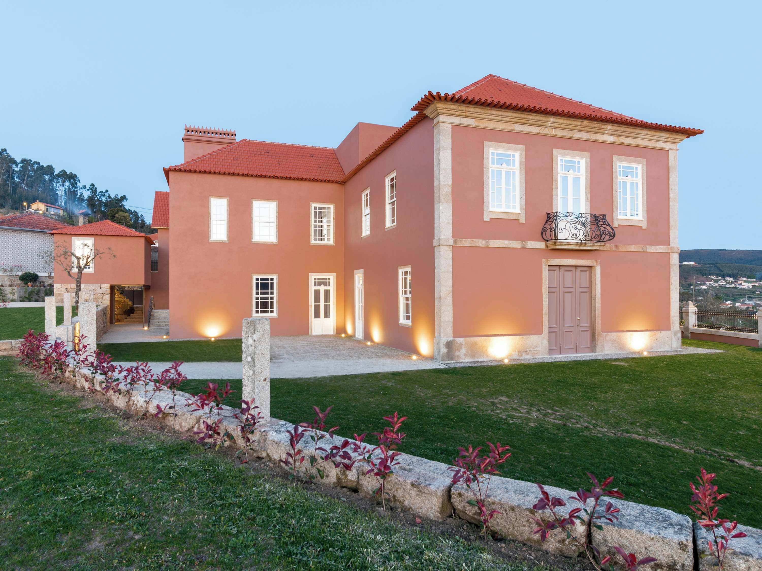 A two-story building with a red-tiled roof, multiple windows, and a stone pathway leading to the entrance.