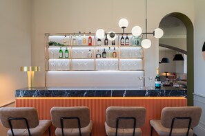 A bar area with a marble countertop, shelves with bottles and glasses, and a seating area with chairs.