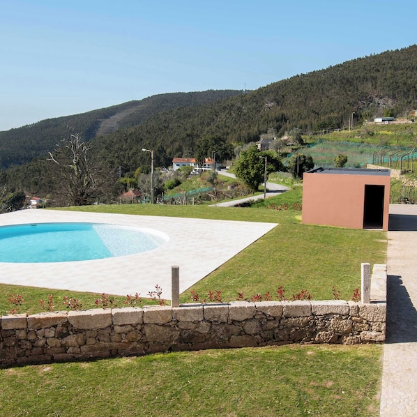 Ein Pool mit Steinmauer, einer Rasenfläche und einem Gebäude im Hintergrund.