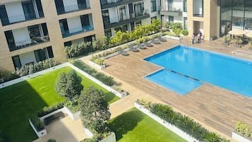 Um edifício moderno com piscina, várias varandas e um jardim bem cuidado.