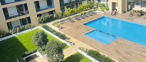 Un edificio moderno con piscina, varios balcones y un césped bien cuidado.