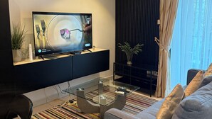 En moderne stue med et fladskærms-tv, et glasbord, en sofa og en stribet måtte.