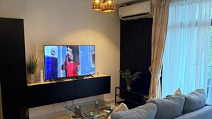 En moderne stue med et fladskærms-tv, en sofa, et sofabord i glas og en stribet måtte.
