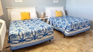 Een kamer met twee bedden, elk met een blauw-wit gebeddeken, witte hoofdborden en een klein nachtkastje met een lamp.