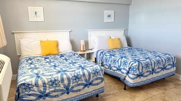 A room with two beds, each with a blue and white patterned bedspread, white headboards, and a small bedside table with a lamp.
