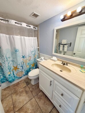 Une salle de bain avec un rideau de douche à motifs marins, un lavabo avec un miroir et des toilettes.