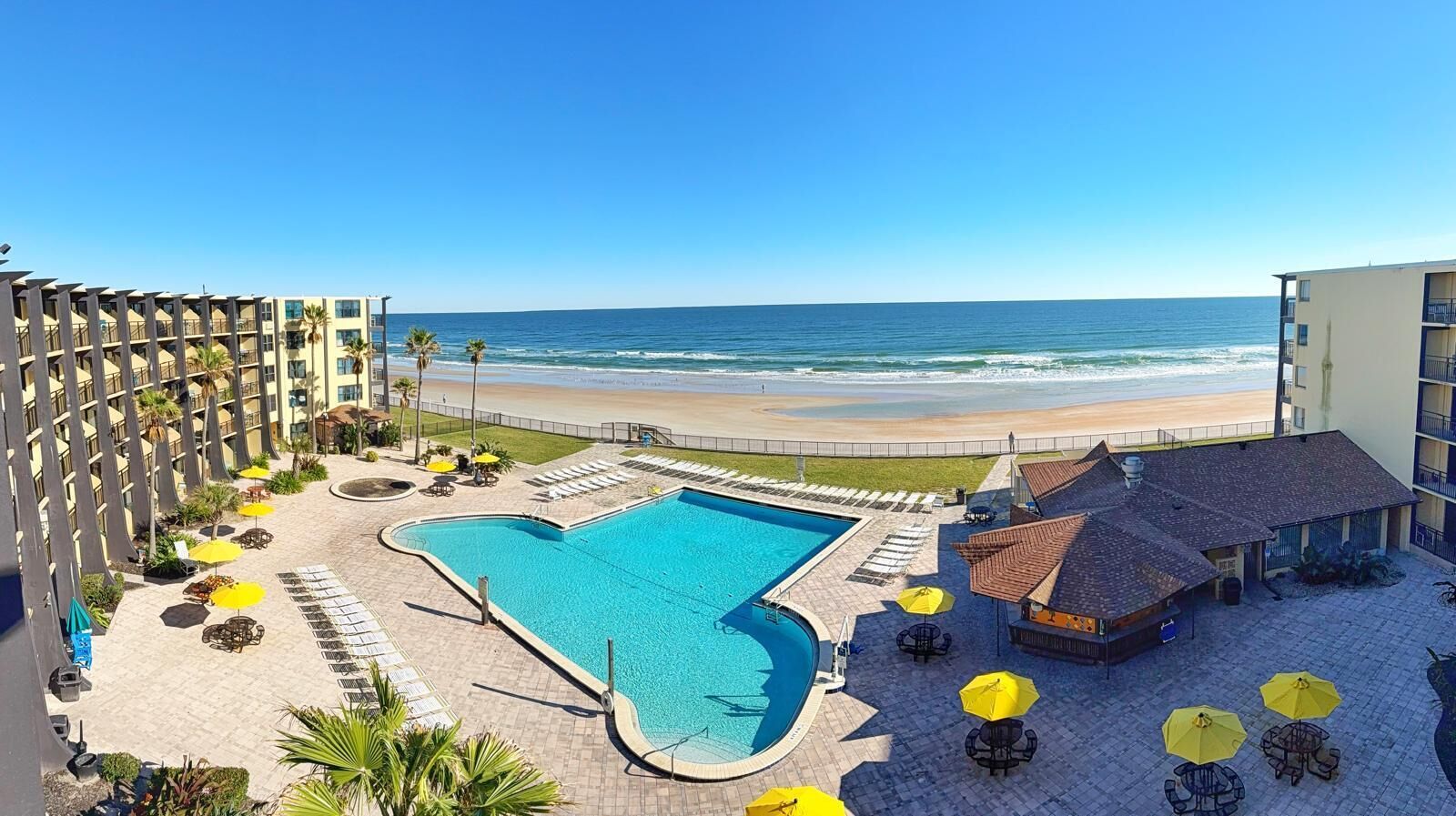 A hotel pool area with a view of the beach, sun loungers, and umbrellas.