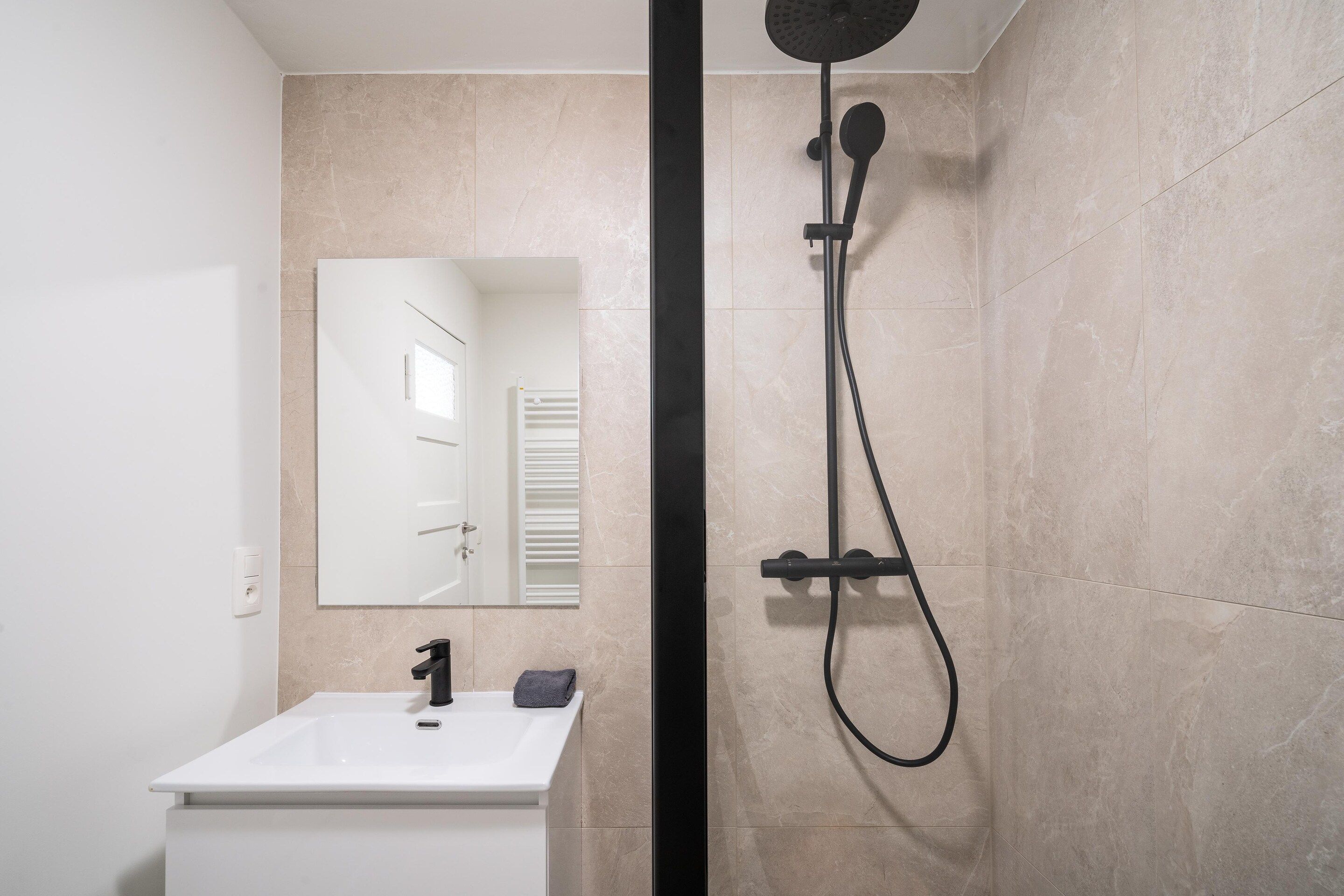 Une salle de bain moderne avec un lavabo blanc, un miroir et une douche équipée d’un pommeau de douche à main.