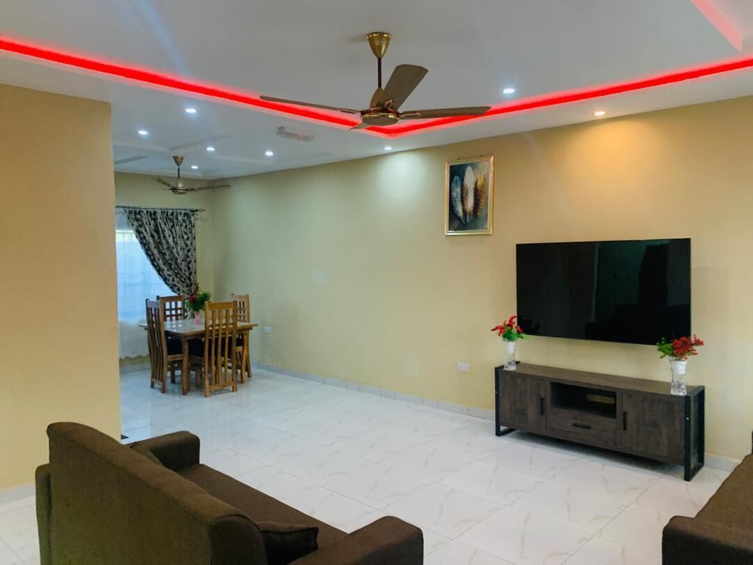 A living room with a flat-screen TV, a ceiling fan, and a dining area with a table and chairs.
