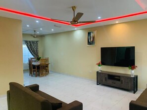 Una sala de estar con una televisión de pantalla plana, un ventilador de techo y un comedor con mesa y sillas.
