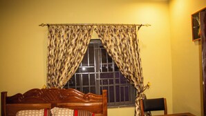Un dormitorio con una cama de madera, una ventana con cortinas estampadas, una mesita de noche y una silla.