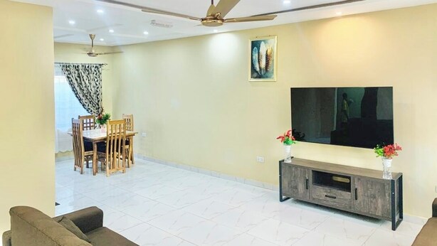 Una sala de estar con sofá, televisor sobre un mueble, ventilador de techo y comedor con sillas y mesa.