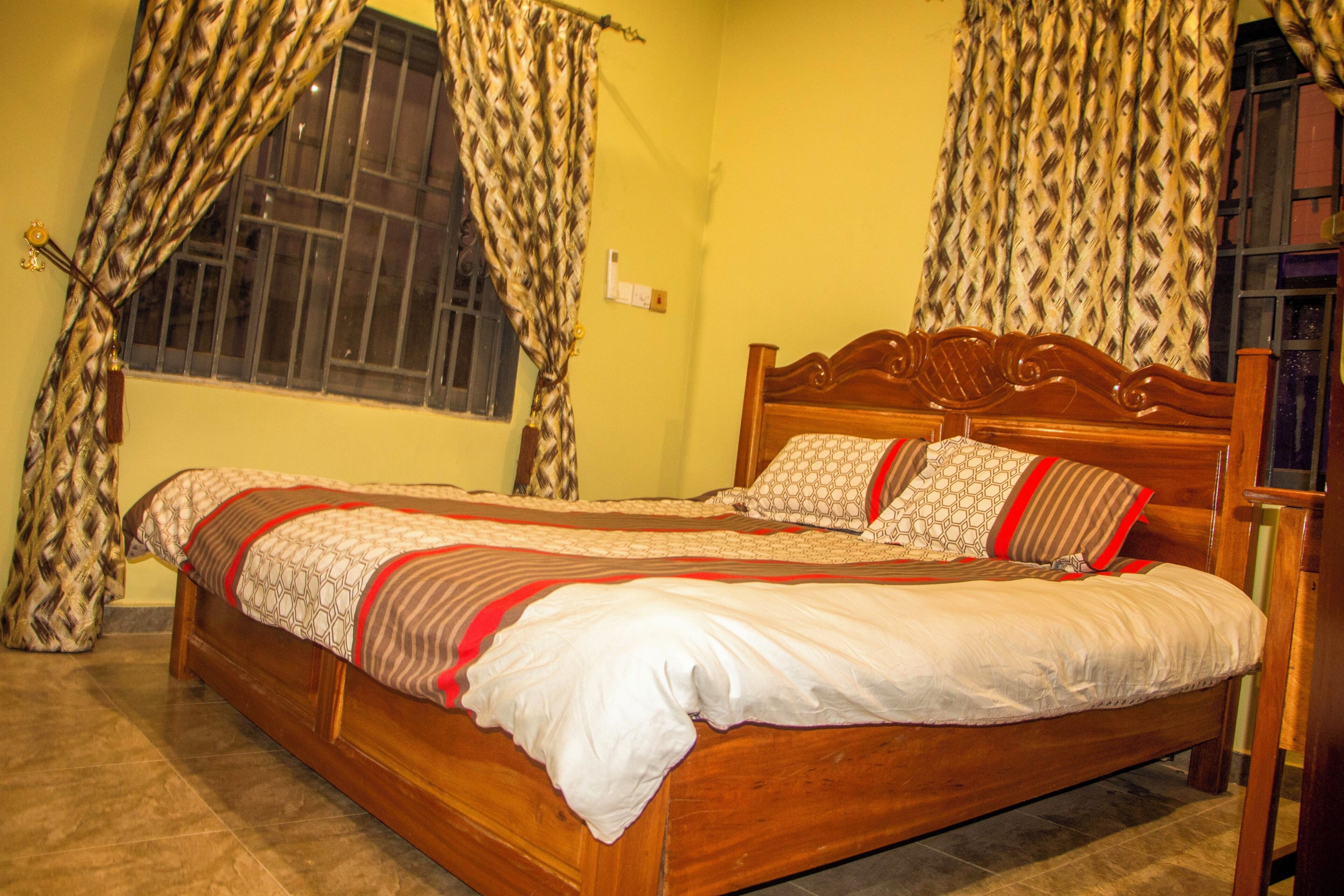 A bed with a wooden headboard, a patterned bedspread, and a window with barred glass.