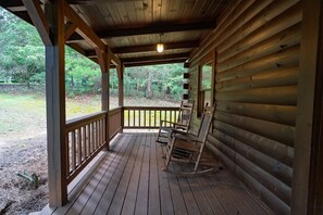 Una baita in legno con veranda, sedie a dondolo e vista sulla foresta circostante.