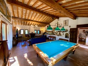 Una mesa de billar en una habitación con vigas de madera, una lámpara colgante y un atril para billar.