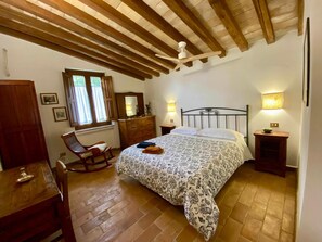 Un dormitorio con cama, muebles de madera, ventilador de techo y ventana con cortinas.