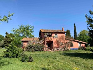 Una casa de dos pisos con techo de tejas, rodeada de un campo cubierto de césped y árboles.