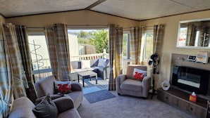 A furnished living room with a sofa, armchair, and a television. - A Stunning High Spec 6 Berth Caravan by the sea (Rhyl)