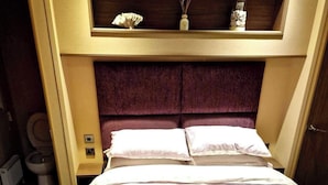 A hotel room with a bed, a headboard, a small shelf with decorative items, and a toilet. - A Stunning High Spec 6 Berth Caravan by the sea (Rhyl)