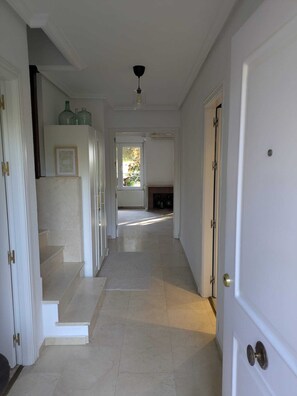 Un pasillo con una escalera, una puerta y vista a una habitación con chimenea.