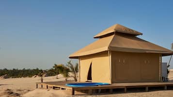 A desert tent with a wooden deck and a blue pool.