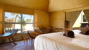 A room with a bed, wooden chairs, a small table, and a view of palm trees. - OKAI - oasis du desert  (Lompoul)