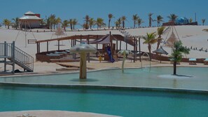 A pool area with a slide, lounge chairs, and palm trees.