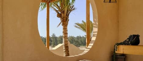 Una habitación con ventanal circular, un banco, una mesita y una lámpara colgante.