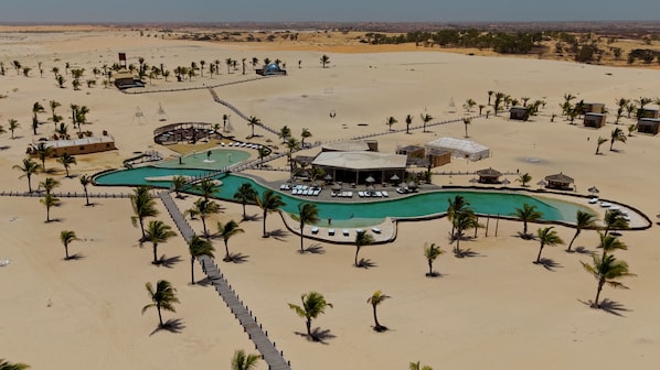 Um resort com piscina, palmeiras e paisagem desértica.