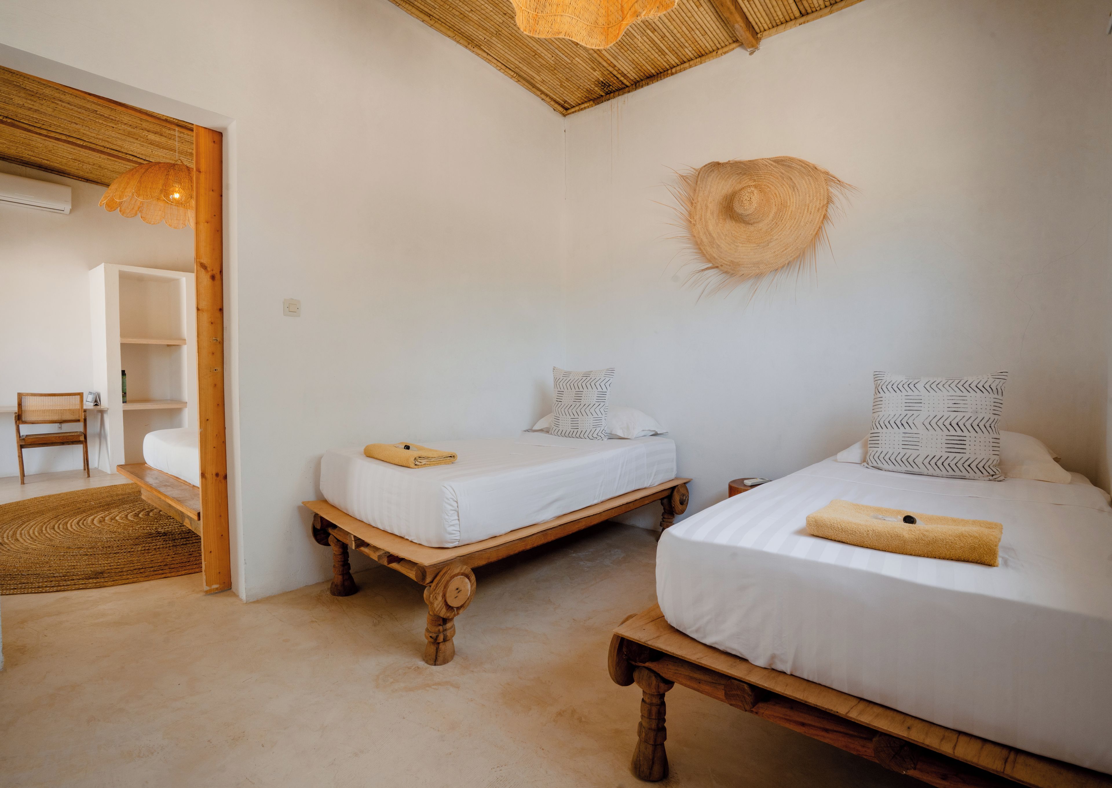 A room with two wooden beds, a woven hat on the wall, and a chair in the corner.