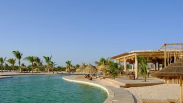 A resort pool area with a curved edge, palm trees, and thatched-roof structures.