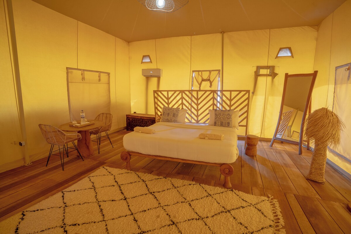A room with a bed, a small table, chairs, a mirror, and a wall-mounted air conditioner.