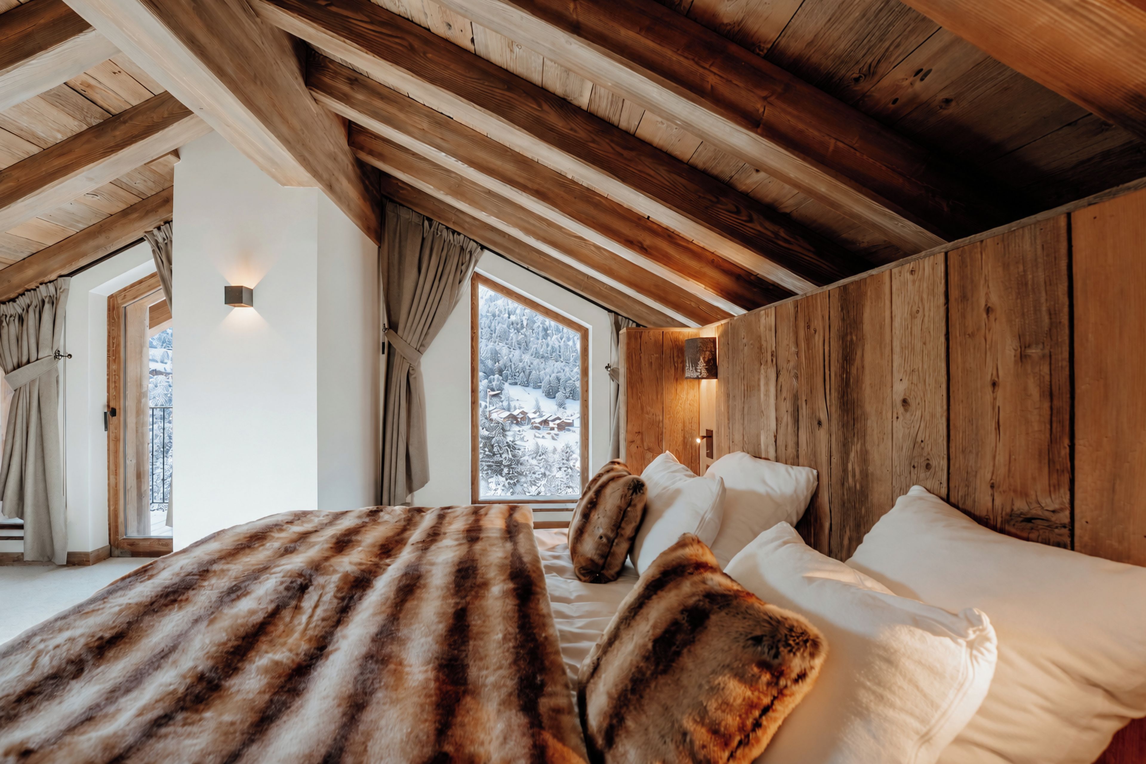A bedroom with a wooden ceiling, a large window with a view of snow-covered trees, and a bed with white bedding.