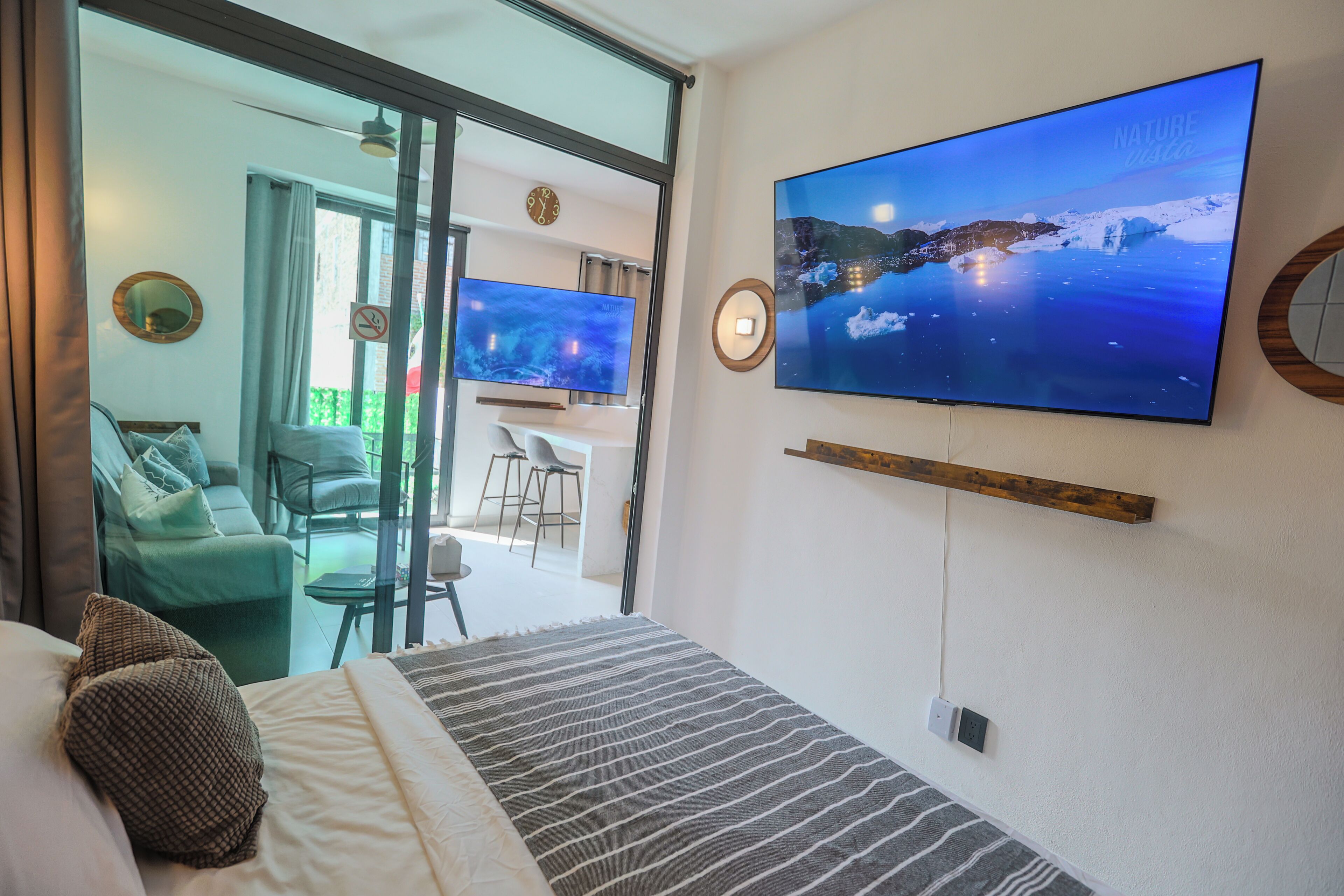 A hotel room with a bed, a TV mounted on the wall, a desk, and a view of the outdoors.