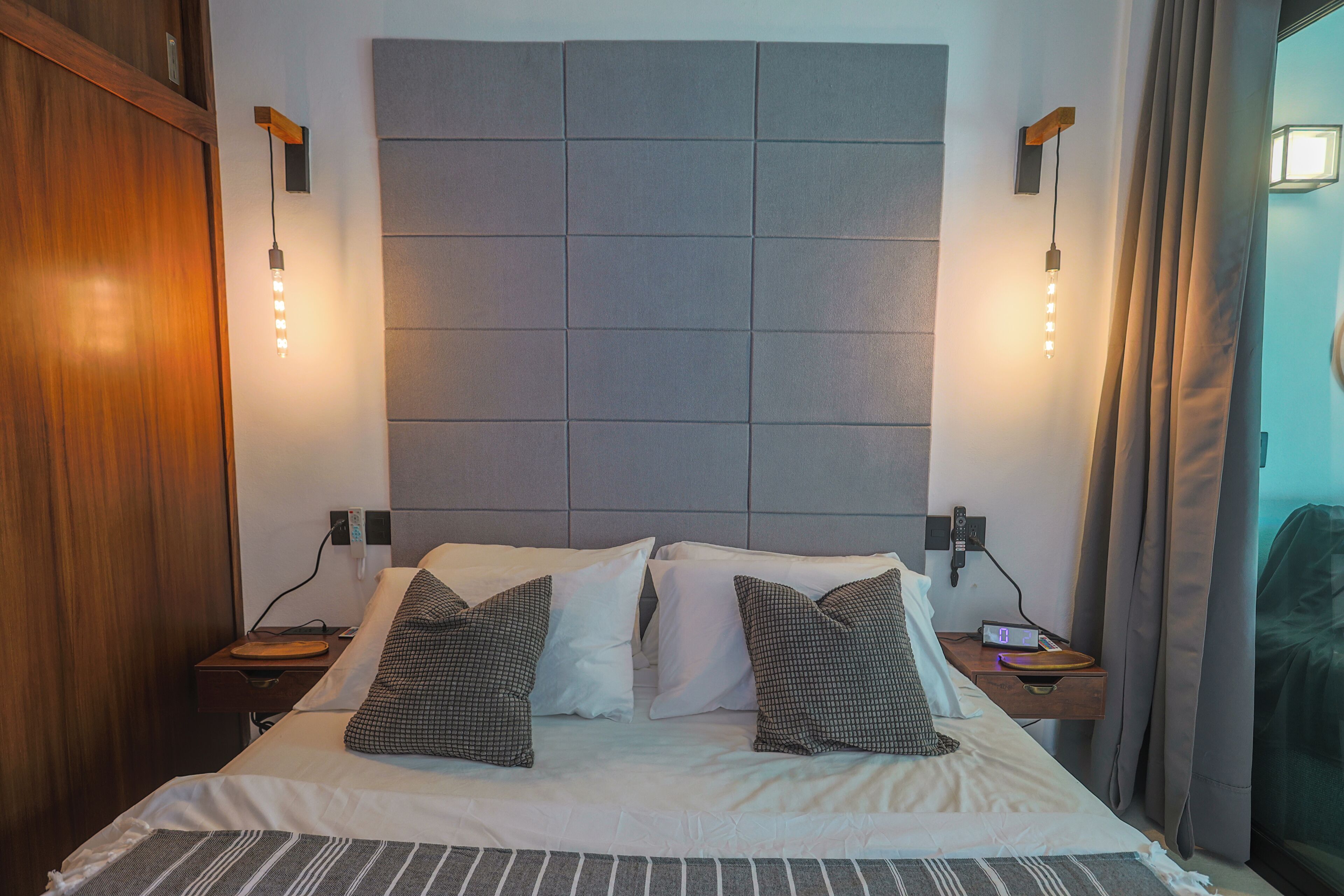 Habitación de hotel con una cama grande, dos mesitas de noche, un cabecero y una lámpara de pared.